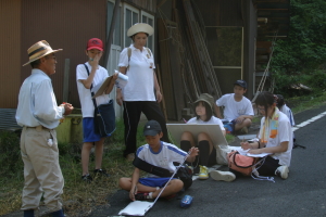 地元住民(左)から「人情調べの石」の説明を聞く探検隊