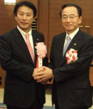 市長在職20年を超え総務大臣表彰を受賞し、樽床伸二総務大臣と握手をする速水市長（10月5日、全国町村会館（東京都））