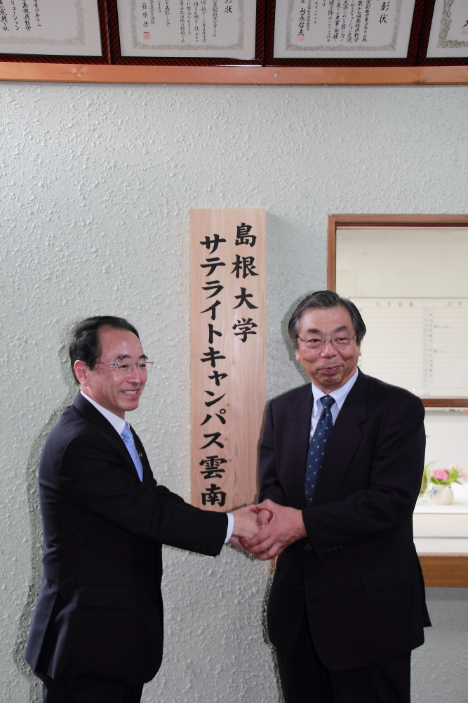 設置した看板の前で握手する、島根大学の小林学長と速水市長の写真