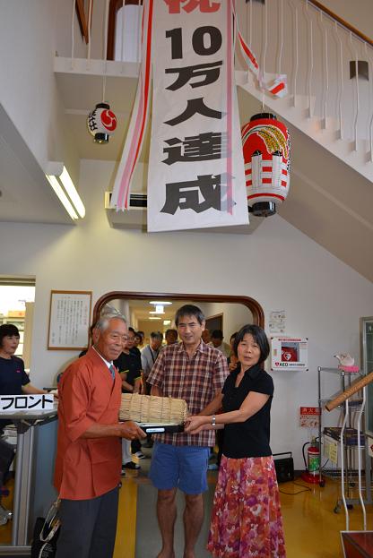 10万人目の重本さんに宮川会長が記念品を手渡す写真