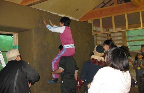 肩車をして素手で泥を壁に塗りこんでいる参加者の写真