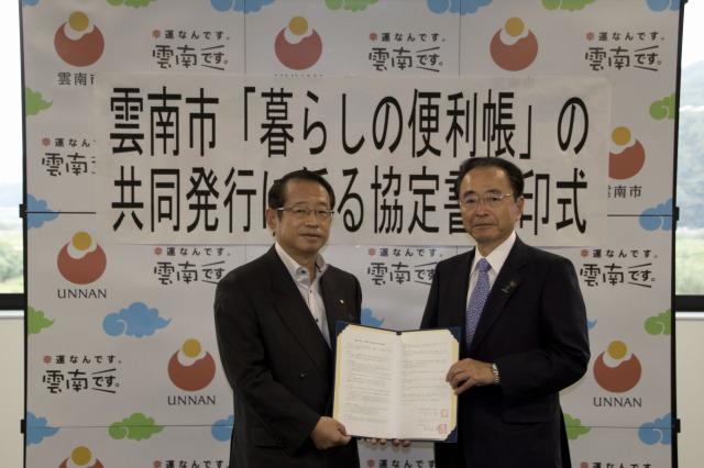 協定調印書を持ち記念撮影する村田社長と速水市長